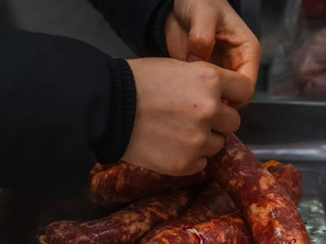 Szakember kolbászt köt és fűszerez a feldolgozóüzemben